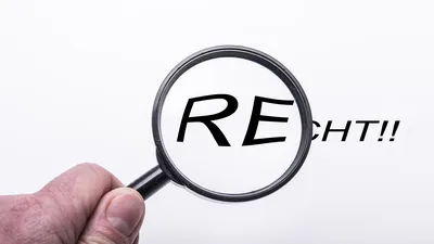 Hand hält Lupe über Text "Recht"