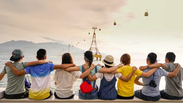 eine Gruppe von Jugendlichen sitzt mit dem Rücken zur Kamera auf dem Boden und schaut aufs Meer