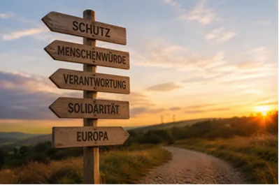 Quelle: KI-generiert mit ChatGPT Feldweg bei Sonnenuntergang, im Vordergrund ein Wegweiser. Ausgeschildert sind "Schutz", "Menschenwürde", "Verantwortung", "Solidarität" und "Europa"