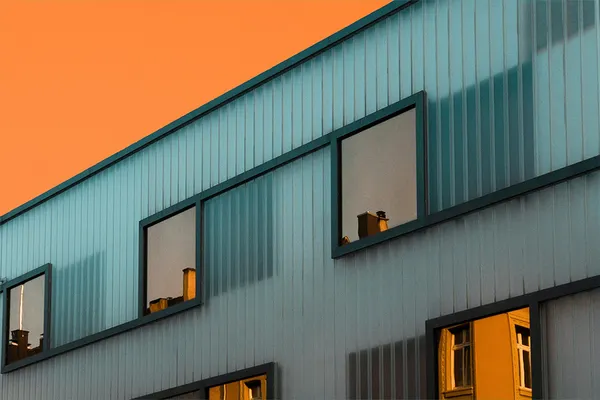 grün-bläuliche Häuserfassade, ein stück orangeleuchtender Himmel, Soiegelungen anderer Häuser in den Fenstern