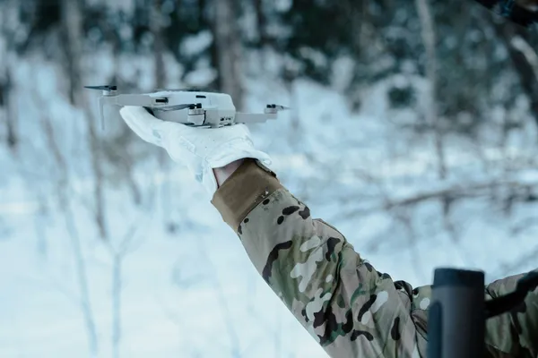 Quelle: Frederick Shaw, Unsplash Winterlandschaft, eine Person in Flecktarnuniform hält eine kleine Drone in der Hand