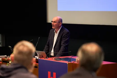 Quelle: Hochschule Offenburg, Hochschule Offenburg Stephan Trahasch hält einen Vortrag. Ein Mann mit dunklem Haar trägt einen dunklen Anzug